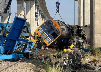 ​ပုံစာ - ကရိန်းနဲ့တိုက်မိပြီးနောက် တိမ်းမှောက်သွားသည့်ရထားအား တွေ့ရစဉ်။ (ဓာတ်ပုံ - EPA)